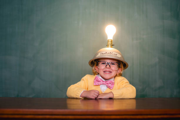 A young nerd girl has a bright idea with copy space in front of a chalkboard. Her lightbulb helmet helps her think of the next big idea.