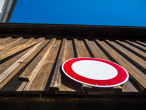 Extreme bottom view of the no-passing traffic sign on a wood-paneled driveway in Bavaria against a blue sky.