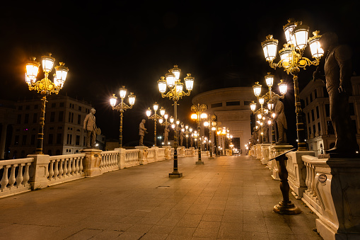 Skopje, North Macedonia,5-1-2023: Illuminated Art bridge of the Skopje Most na umetnosta at night with lighted lamps on the river Vardar selective focus background blur noise