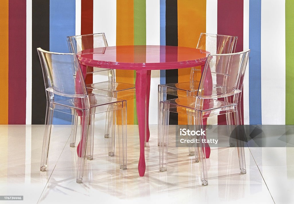 Lucite chairs and a pink table against colorful stripes Transparent plastic chairs inside colorful interior with stripes wall Chair Stock Photo