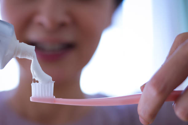 An older asian woman with cancer brushes her teeth at home while going through anticancer treatment.