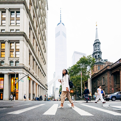 Full length side view of young professional in work attire returning to office from coffee break, One World Trade Center and St. Paul’s Chapel in background.