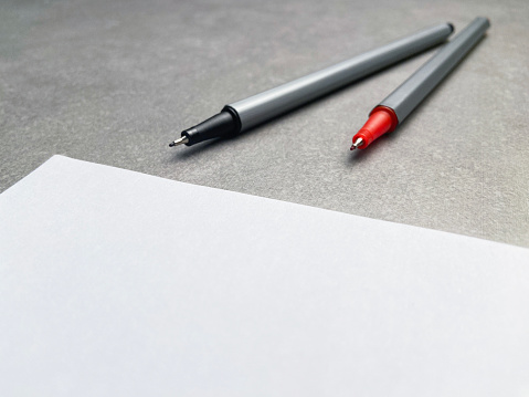 A blank white paper, red and black pens on gray stone table background