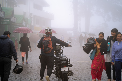 Darjeeling, India - 22nd Aug 2023: man dragging motor bike on mall road in Darjeeling on which vehicles are not allowed as onlookers enjoy the foggy weather