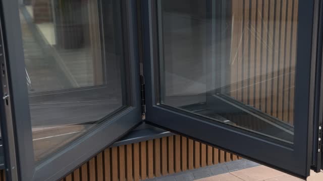 Close up shot of somebody opening sliding bi fold patio doors in slow motion on luxury wooden garden room with cladding and with reflections in the glass