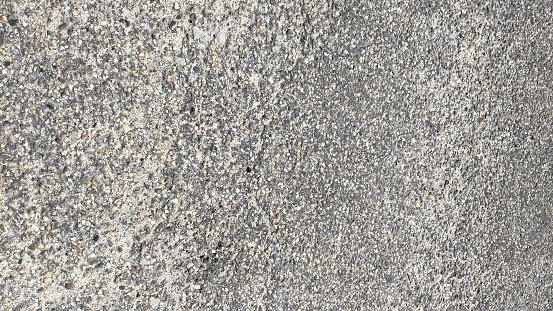 A close-up of an asphalt road abstract texture background reveals a rich, detailed, and complex surface. Asphalt, also known as bitumen is commonly used in road construction, where it acts as a binder mixed with aggregate particles to create asphalt concrete. The texture of the asphalt road is greyish in color, it is rough and uneven, with small stones, or aggregates, embedded in the bitumen binder. These stones vary in size, creating a varied texture that can range from relatively smooth to quite rough. The color of the asphalt vary from light to dark grey