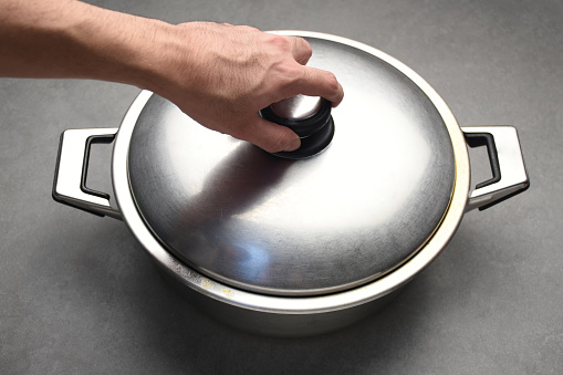 A hand opening a stainless steel saucepan lid