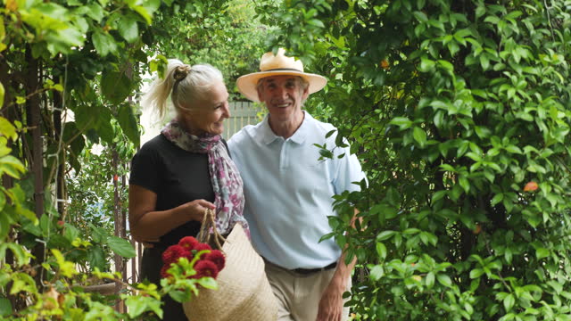 Happy senior couple with flowers walking under trellis in garden