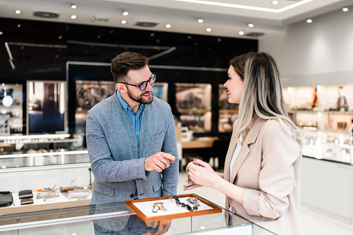 Elegant middle age businessman choosing and buying his new expensive watch. Beautiful youg female seller helps him to make good decision. Fashion style and elegance concept.