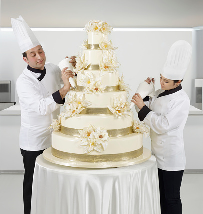 Pastry chefs piping and completing wedding cake in a commercial kitchen