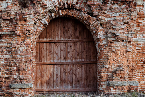 A powerful wooden door is closed, an arched passage in the wall of an old building, an ancient castle is built of red brick, a ruined structure. High quality photo
