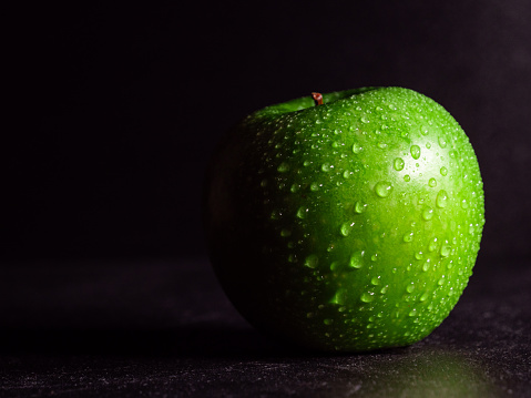 A delicious green apple with water drops against a black background
