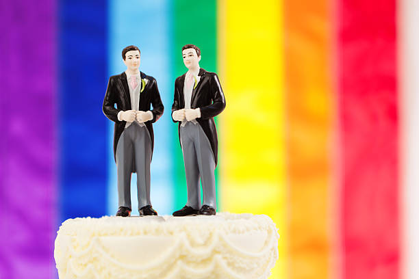 Same Sex Marriage Wedding Cake with Rainbow Flag Subject: Same sex marriage wedding cake with two male groom figurine cake toppers and rainbow flag in background. civil partnership stock pictures, royalty-free photos & images