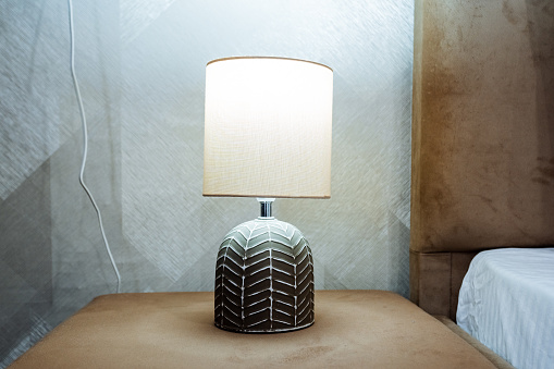 The lamp stands on the bedside table, the night light illuminates the room, bedside reading light, white sconces, ceramic lamp, light bulb design. High quality photo