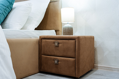 Bedside table with two drawers, Evening light lamp in the bedroom, designer furniture, finishing of the bedside table with soft material, furniture in the house. High quality photo