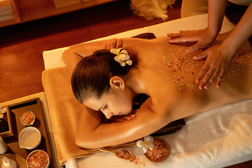 Woman customer having exfoliation treatment in luxury spa salon with warmth candle light ambient. Salt scrub beauty treatment in Health spa body scrub. Quiescent