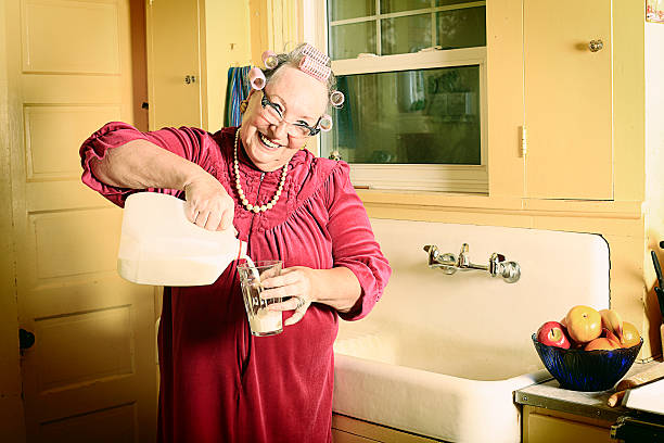 Granny in Kitchen Pouring Milk A granny in curlers and cat's eye glasses in her kitchen near the sink pouring a glass of milk. More granny images. retro 1950s kitchen stock pictures, royalty-free photos & images