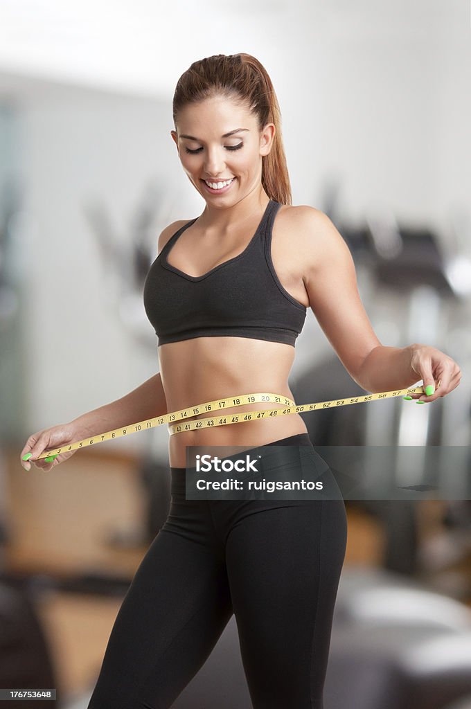 Diet Time Woman measuring her waist with a yellow measuring tape, in a gym Abdomen Stock Photo