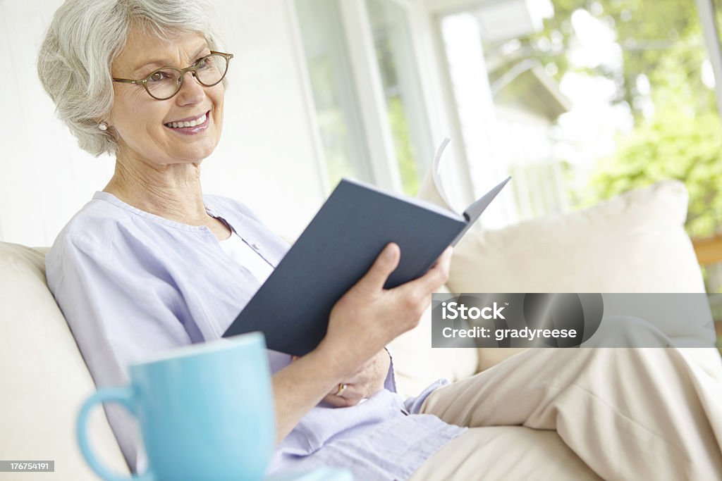 Picturing a scene from her book A beautiful senior woman reflecting on a good book while sitting on her sofa 60-69 Years Stock Photo