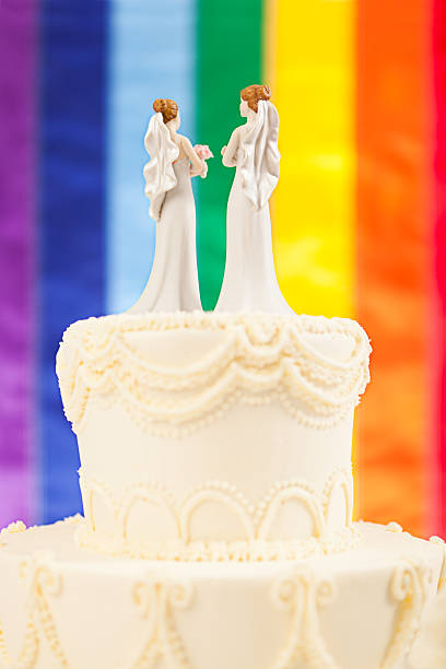 Same Sex Marriage Brides Wedding Cake with Rainbow Flag Subject: Same sex marriage wedding cake with two female bride figurine cake toppers and rainbow flag in background. wedding ceremony formalwear people clothing stock pictures, royalty-free photos & images