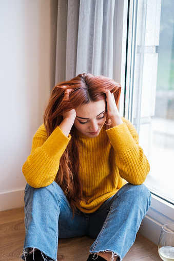 A beautiful young woman is sitting on the sofa by the window on a cold winter day.