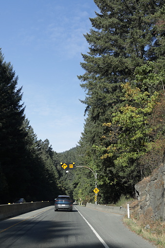 Langford, Canada - September 17, 2023: Traffic heads northwest on Highway  1 through the West Coast forest of Goldstream Provincial Park. Summer day with light clouds over Vancouver Island.
