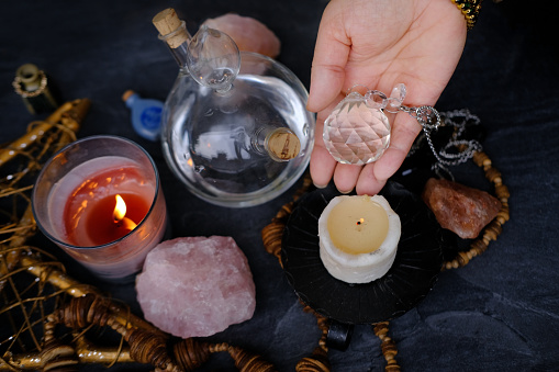 Spiritualistic Salon Experience, esoteric table, female fortuneteller's hand holding and using glass ball crystal, candles burn, concept of magic, Secrets of Witchcraft