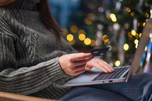 Christmas online shopping, sales and discounts promotions during winter holidays, online shopping at home. Female hands on the laptop with credit card and blurred bokeh lights