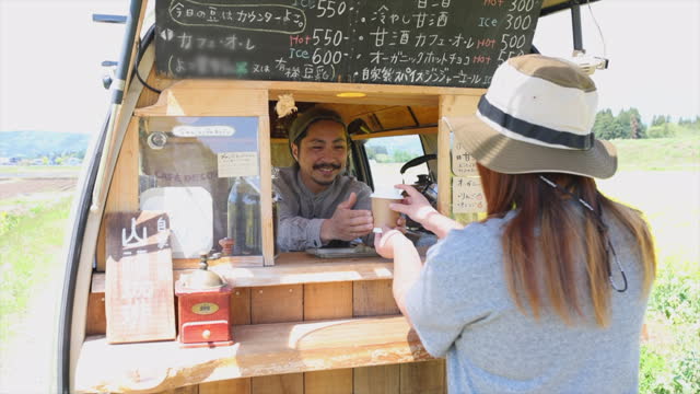 Japanese man selling coffee from his van in the countryside with canola flowers