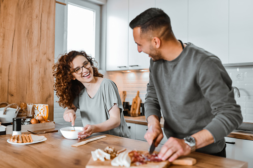 Smiling Couple Utilizing Teamwork While Preparing Omelette At Home