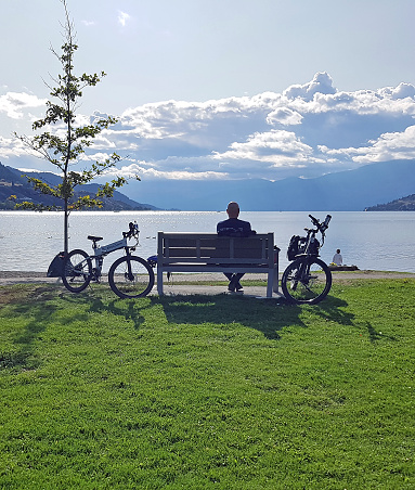 Vernon, British Columbia, Canada- September 30, 2023:  Man and woman  with electric bikes parked and sitting by Lake Okanagan in Vernon BC. Autumn season.