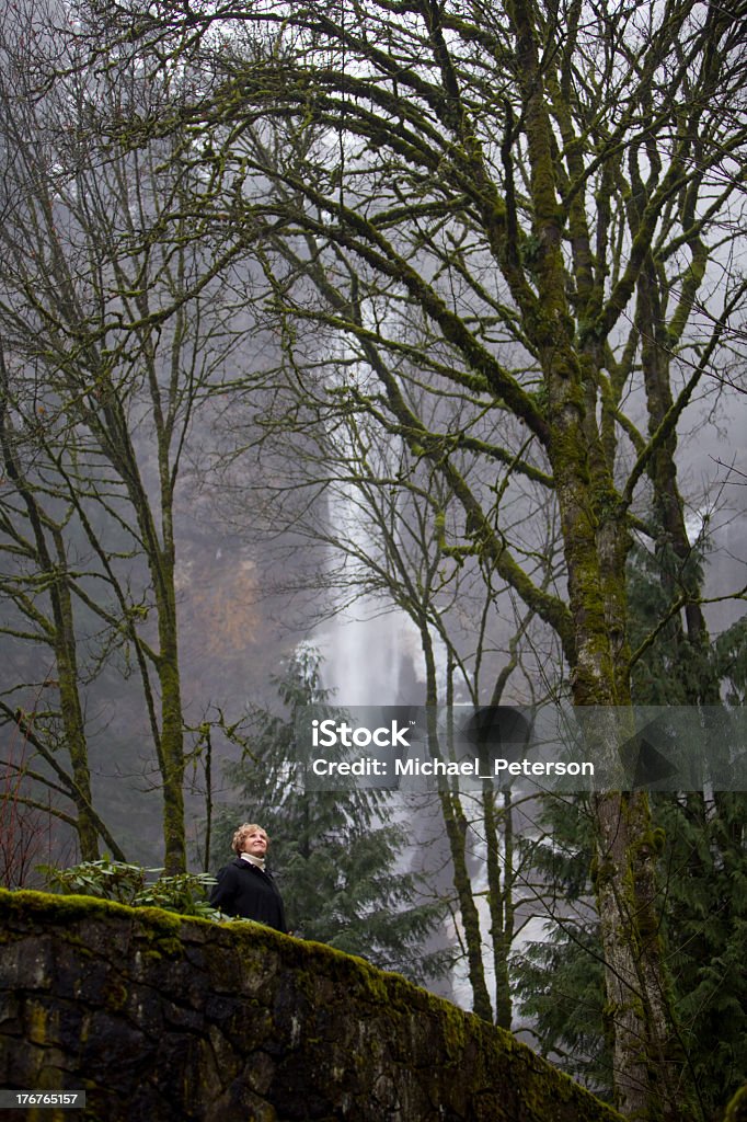 Senior Woman and Waterfall Senior woman standing on a large rock wall looking at the scenery with a partially frozen waterfall in the background.  Image was taken at Multnomah Falls in the state of Oregon, USA. AARP Stock Photo