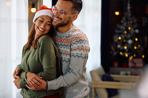 Young happy couple embracing while spending Christmas together at home.