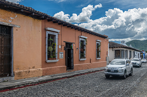 Guatemala, La Antigua - July 20, 2023: Calle Poniente. Bistrot Cinq entrance and red facade with windows. Street scene with cars under blue cloudscape