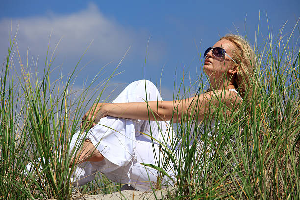 Beautiful blonde girl sitting on a sand in dunes stock photo