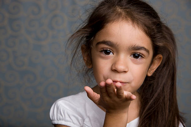 A head and shoulder portrait of a smiling Hispanic little girl blowing a kiss.