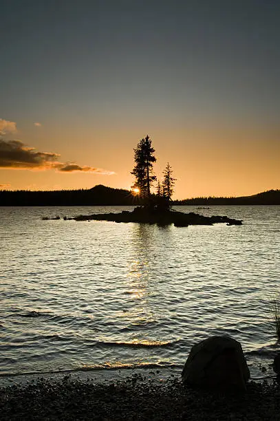 "Island silhouette on Waldo Lake 1650m (5,414ft), with sunset over Klovdahl Bay.  Viewed from Shadow Bay on the east shore.  A group of five silhouetted and unidentifyable kayakers is rafted up enjoying the sunset."