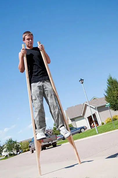 Teenage boy walking around the neighborhood on stilts.