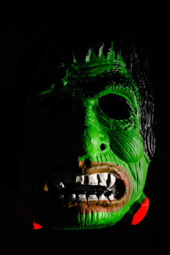 A 1950's era Halloween Mask of a green monster's face on a black background