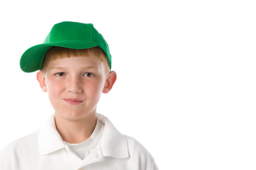 A caucasian redhead  little boy wearing a green baseball cap and a smirk or smile.