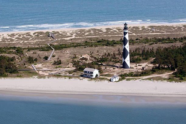 Cape Lookout Lighthouse Aerial The Cape Lookout Lighthouse is a 163-foot high lighthouse located on the Southern Outer Banks of North Carolina. It flashes every 15 seconds and is visible at least 12 miles out to sea and up to 19 miles. The Cape Lookout Light is one of the very few lighthouses that operate during the day. It became fully automated in 1950. emerald isle north carolina stock pictures, royalty-free photos & images