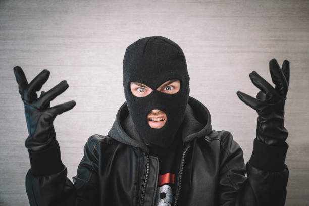 thief in a black jacket. A man in a black balaclava with an evil expression on his face. An aggressive bandit on a white background. The concept of crime or theft. A thief in a black jacket. A man in a black balaclava with an evil expression on his face. An aggressive bandit on a white background. The concept of crime or theft. wrongdoer stock pictures, royalty-free photos & images