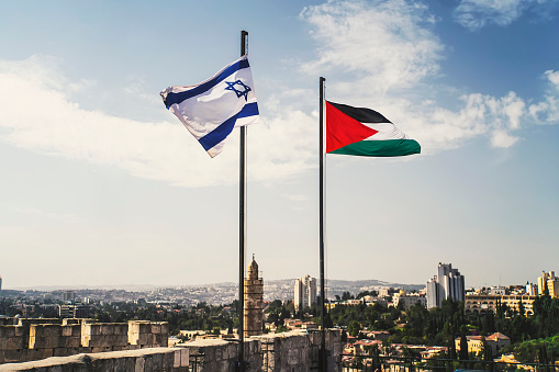 flags of Palestine and Israel against sky and old Jerusalem. Two States for two peoples. Two-state solution concept. Separate ownership of Jerusalem. The division of the city between two peoples. Israel vs Palestine in the West Bank.