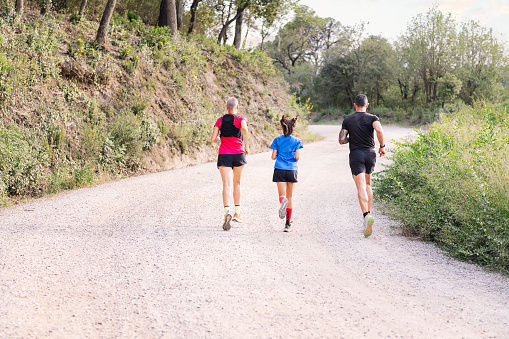 rear view of an unrecognizable sporty family running in the countryside, concept of sport in nature with kids and healthy lifestyle, copy space for text
