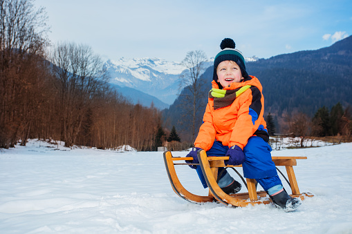 Caucasian boy sledding with sled on the small hill, during a winter day on the mountain