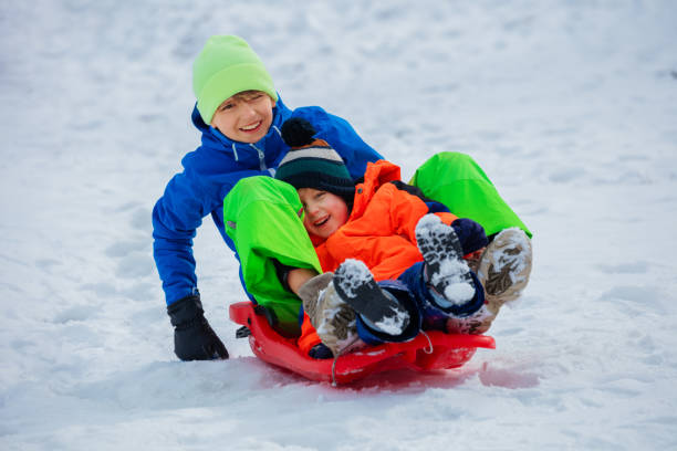 Two happy boys, brother slide downhill on red sledge