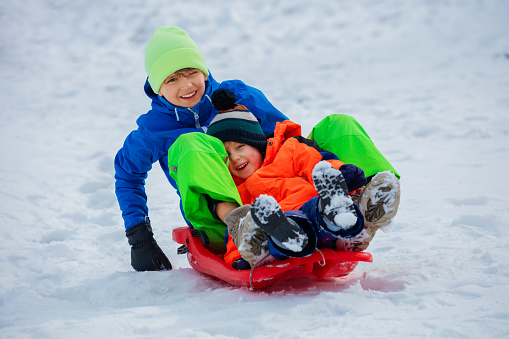 Two happy boys, brother slide downhill on red plastic sledge having fun