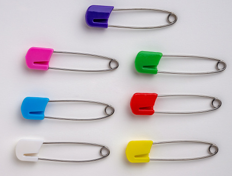 Seven colourful diaper safety pins on a white Background
