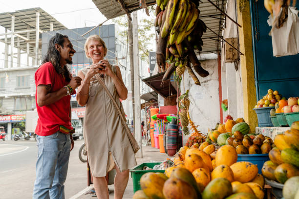 ein sri-lankischer mann, ein führer, hilft einer europäischen touristin, 50-jährige aktive frau, frische reife früchte auf einem lokalen straßenmarkt in aluthgama, sri lanka zu pflücken - 30s women asian ethnicity 35 40 years stock-fotos und bilder