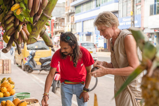 ein mann aus sri lanka hilft einer europäischen touristin, einer 50-jährigen aktiven frau, auf einem lokalen straßenmarkt in aluthgama, sri lanka, frische, reife früchte zu pflücken. - 30s women asian ethnicity 35 40 years stock-fotos und bilder